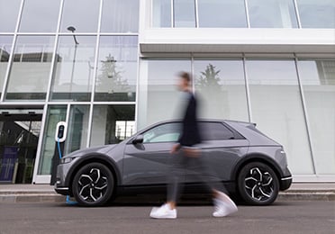Egy férfi egy modern épület előtt parkoló elektromos autó mellett sétál