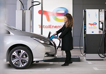 Egy elektromos autót töltő hölgy a TotalEnergies nyilvános töltőállomásán
