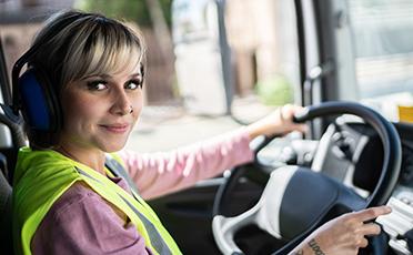Egy járművezető nő fényvisszaverő mellényben egy kamion volánja mögött