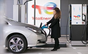 Egy nő kabátban az elektromos autóját tölti a TotalEnergies töltőállomásán