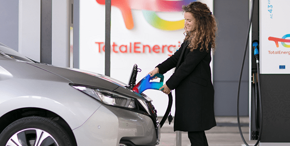 Egy kabátos nő tölti fel elektromos autóját a TotalEnergies töltőállomásáról